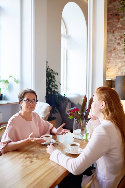 Две женщины-коллеги, взаимодействующие за чашкой кофе в кафе
 - Фото, изображение