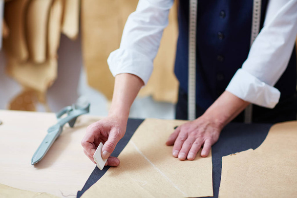 Portrait d'un tailleur qualifié méconnaissable travaillant en atelier : tracer des motifs sur tissu à la craie
 - Photo, image