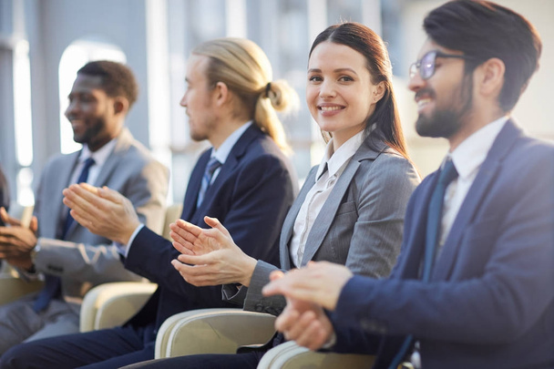 Young businesswoman looking at camera while applauding to speaker at conference - Photo, Image