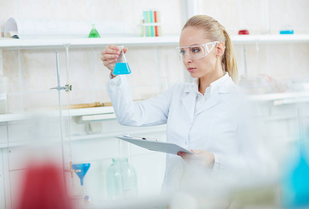 Portret van mooie vrouwelijke scheikundige bezig met onderzoek in moderne laboratorium holding reageerbuisjes - Foto, afbeelding