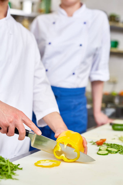 Шеф-кухар ресторану нарізає свіжий перець з учнем поруч
 - Фото, зображення