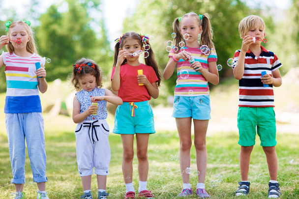 夏の子供服緑の芝生の上の行に立って、シャボン玉を吹いて - 写真・画像