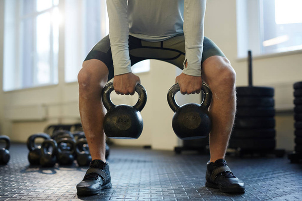 Portrait en coupe basse d'un homme méconnaissable soulevant deux lourdes kettlebells avec un effort vigoureux pendant l'entraînement sur la salle de gym
 - Photo, image