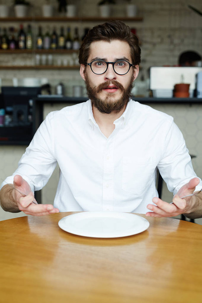 Giovane uomo in camicia bianca seduto al tavolo in caffè con piatto vuoto
 - Foto, immagini