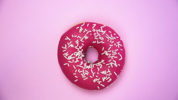Delicious sweet donut rotating on a plate. Top view. Bright and colorful sprinkled donut close-up macro shot spinning on a pink background. - Footage, Video