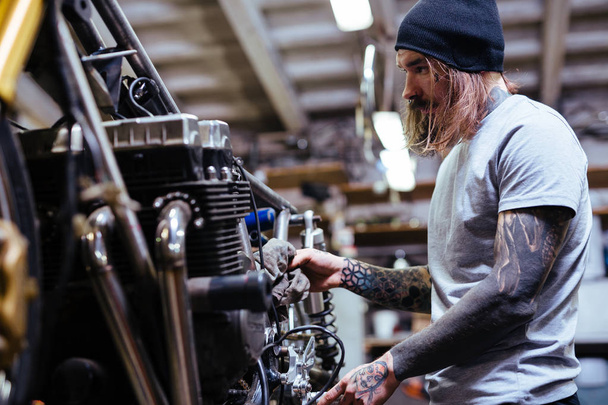 Portrait d'un homme tatoué travaillant dans un garage réparant une moto cassée et la personnalisant
 - Photo, image
