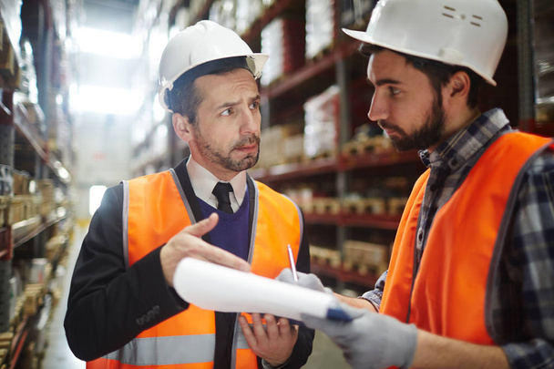Portrait of warehouse worker talking to supervising manager while doing inventory control in entrepo - Photo, Image