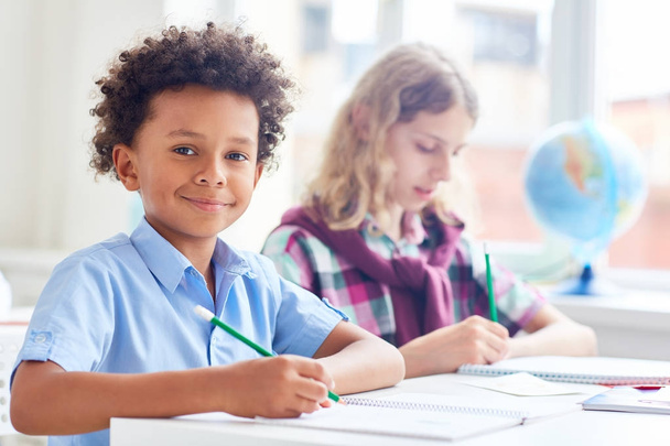 Усміхнений школяр з олівцем пише есе або готує домашнє завдання
 - Фото, зображення