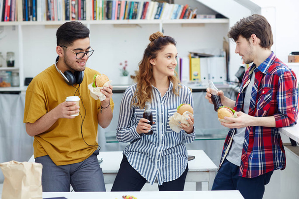 Дружелюбные студенты с напитками и сэндвичами разговаривают во время обеденного перерыва
 - Фото, изображение
