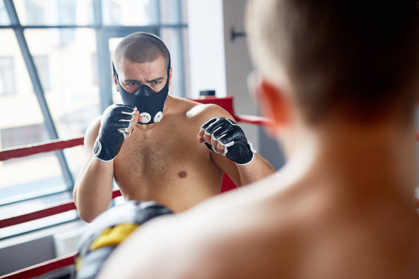 ボクシングのリングで対戦相手と戦う持久力トレーニング マスクを身に着けている若いボクサーの肖像画 - 写真・画像