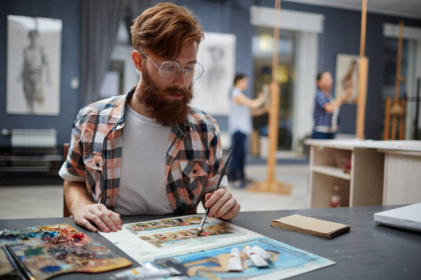 Portrait of contemporary bearded artist working in art studio painting oil pictures looking focused and concentrated - Photo, Image