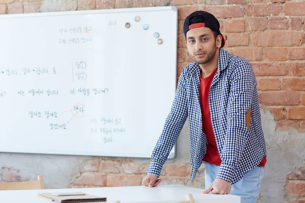 Young learner in casualwear leaning against desk by whiteboard in classroom - Photo, Image