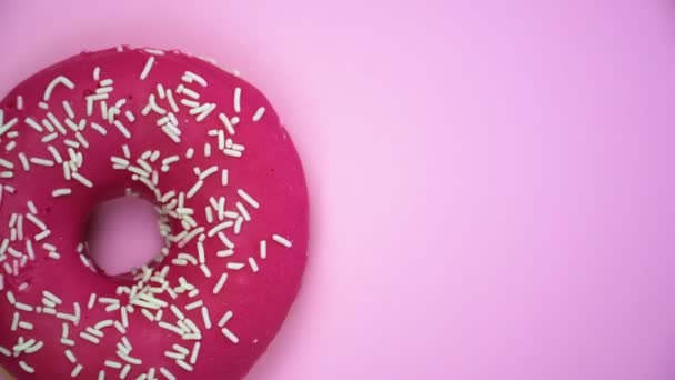 Heerlijke zoete donut draaien op een plaat. Bovenaanzicht. Helder en kleurrijk bestrooid donut close-up macro geschoten spinnen op een roze achtergrond. - Video