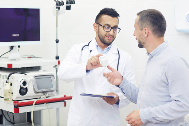 moderner Arzt in Uniform zeigt dem Patienten während des Termins neue Medikamente - Foto, Bild