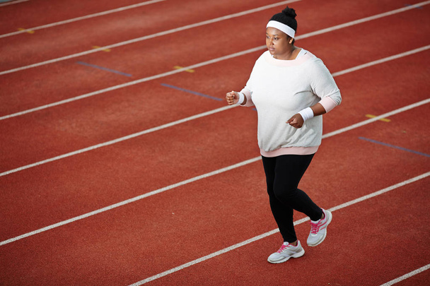 Determined overweight African woman jogging on running track to lose weight - Photo, Image