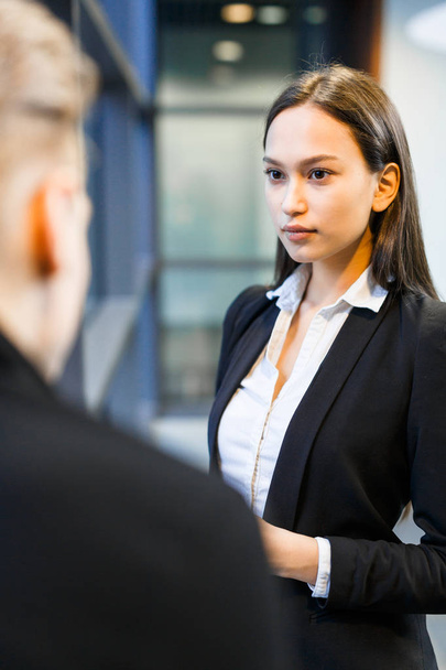 Attractive mixed race entrepreneur looking at her business partner with concentration while discussing details of their agreement, over shoulder view - Фото, зображення