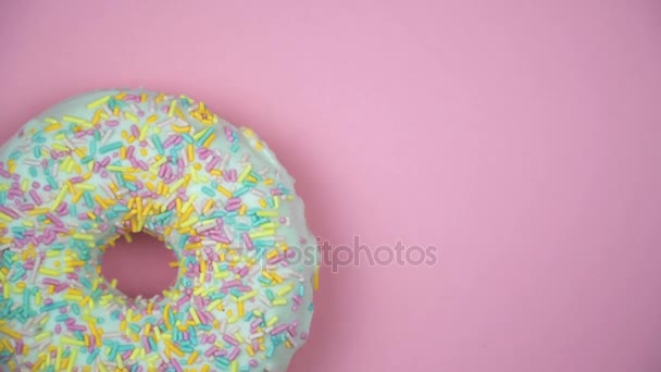 Delicious sweet donut rotating on a plate. Top view. Bright and colorful sprinkled donut close-up macro shot spinning on a pink background. - Footage, Video