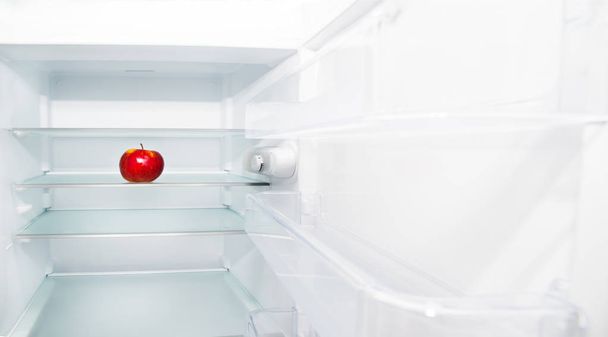 Una mela sana e fresca in frigorifero vuoto. Non c'è niente da mangiare in frigo, il frigo bianco è vuoto, è rimasta solo una mela sana. Concetto di cibo sano
. - Foto, immagini