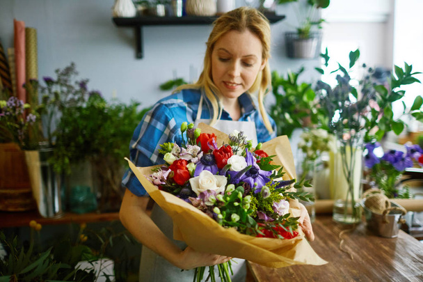 Jovem florista olhando para bouquet arranjado em suas mãos
 - Foto, Imagem