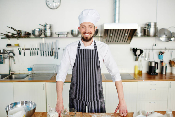 Happy young man in uniform of baker standing by workplace - Photo, Image