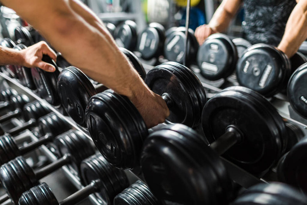 Gros plan du bras masculin musclé ramassant des poids lourds à partir du porte-haltères dans la salle de gym moderne
 - Photo, image