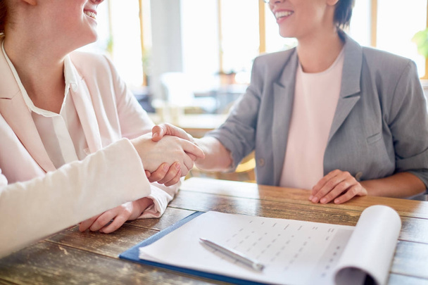 Close-up shot of unrecognizable business partners shaking hands as sign of successful negotiations, clipboard with signed documents on foreground - Foto, Imagen