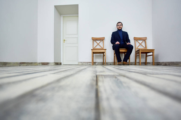 Безробітний чоловік сидить на стільці і чекає своєї черги на співбесіду
 - Фото, зображення