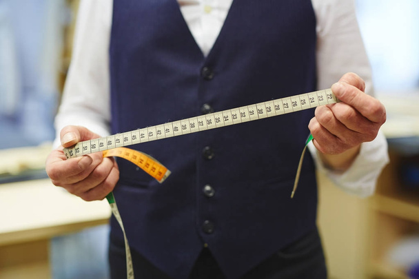 Крупный план неузнаваемого портного, держащего измерительную ленту в руках во время работы в традиционной мастерской ателье
 - Фото, изображение
