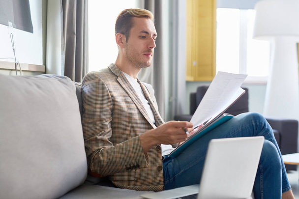 Jeune homme se concentrant sur la lecture de documents financiers ou de contrats à domicile
 - Photo, image
