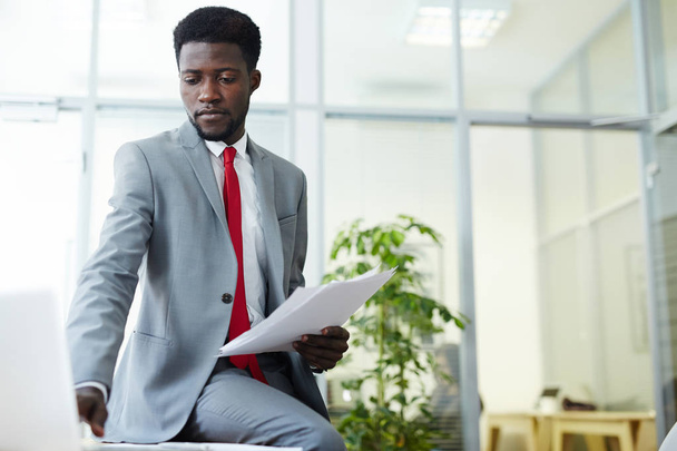 Guapo africano trabajador de cuello blanco estadounidense que usa traje elegante comprobar correos electrónicos de negocios en el ordenador portátil mientras trabaja en una oficina espaciosa
 - Foto, imagen