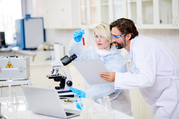 Χαρούμενα ομάδα Μικροβιολόγοι φορώντας ασφάλειας γυαλιά βλέπουν δοκιμαστικό σωλήνα με περηφάνια ενώ εργάζονται από κοινού για δημιουργία νέο εμβόλιο κατά του καρκίνου, εσωτερικό του σύγχρονο εργαστήριο σε φόντο - Φωτογραφία, εικόνα