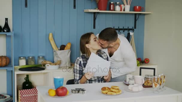 Attractive happy couple recieve good news unfolding letter in the kitchen while have breakfast at home - Video