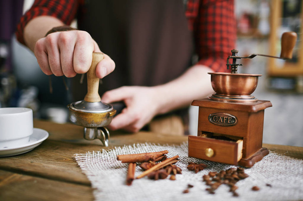 Detailní záběr barista pracuje v kavárně retro: lisování čerstvých zrna s vměšovat po broušení je v antické mlýn - Fotografie, Obrázek