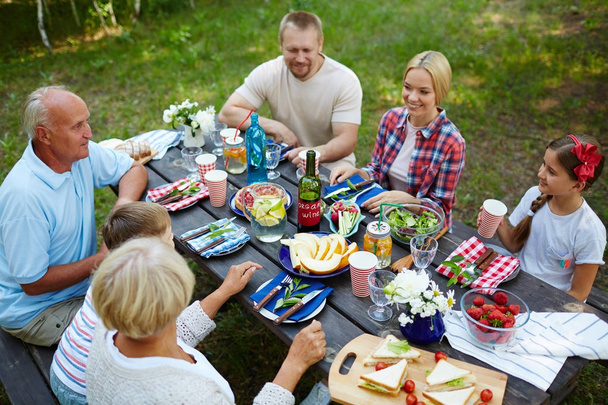 Tres generaciones cenando por mesa servida al aire libre
 - Foto, Imagen