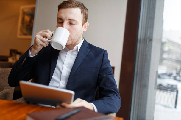 Geschäftsmann mit Tablet trinkt Kaffee aus Becher und sucht im Netz - Foto, Bild