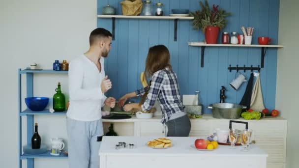 Young joyful couple have fun dancing and singing while set the table for breakfast in the kitchen at home - Video, Çekim