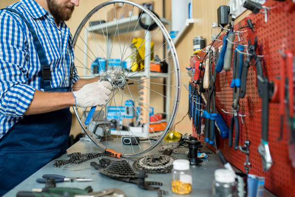 Reparador em pé por seu local de trabalho e parafuso de aperto na roda de bicicleta
 - Foto, Imagem