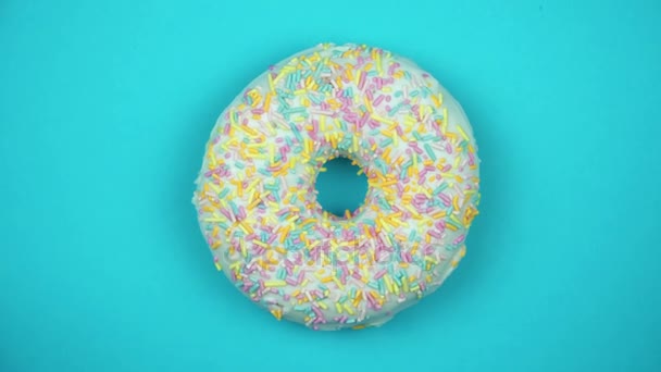 Heerlijke zoete donut draaien op een plaat. Bovenaanzicht. Helder en kleurrijk bestrooid donut close-up macro geschoten spinnen op een blauwe achtergrond. - Video