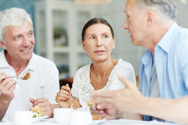 zwei ältere Männer und eine Frau unterhalten sich beim Dessert-Essen im Café - Foto, Bild