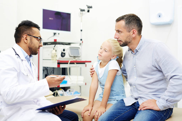 Udzielanie porad dla małej dziewczynki podczas rozmowy z ojcem podczas wizyty lekarz - Zdjęcie, obraz