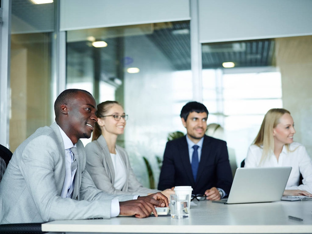 internationale Gruppe junger begeisterter Geschäftsleute lächelt am runden Besprechungstisch im Konferenzraum des modernen Büros - Foto, Bild