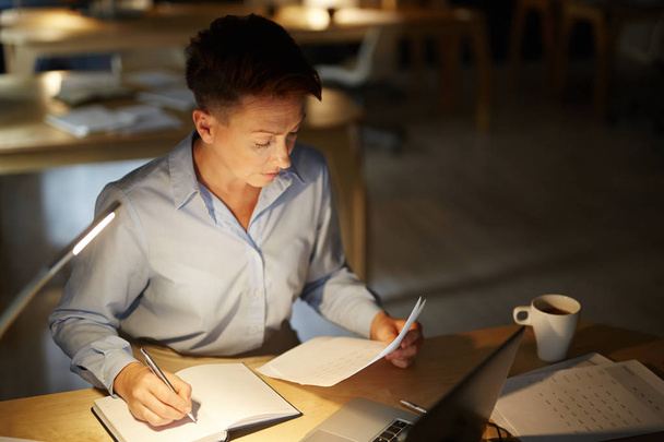 Femme d'affaires sérieuse se concentrant sur la lecture de documents financiers et de prendre des notes dans son carnet
 - Photo, image