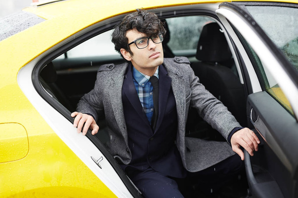 Πορτρέτο του νεαρός επιτυχημένος επιχειρηματίας Μέσης Ανατολής να πάρει έξω από το ταξί για το βροχερό φθινόπωρο δρόμου - Φωτογραφία, εικόνα
