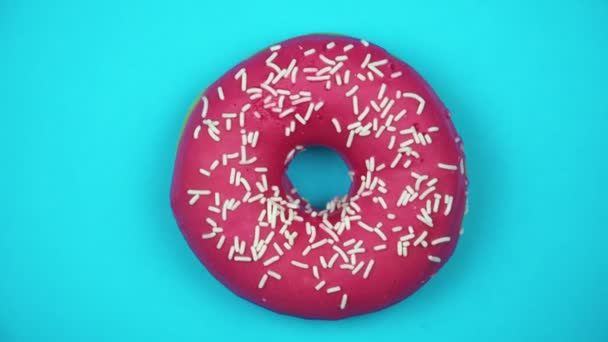 Delicious sweet donut rotating on a plate. Top view. Bright and colorful sprinkled donut close-up macro shot spinning on a blue background. - Footage, Video