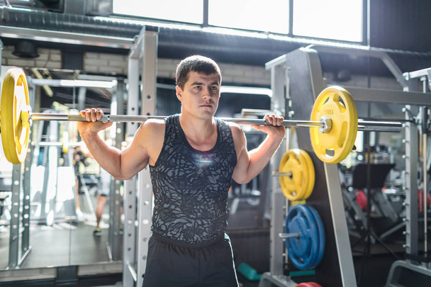 Portret van fit gespierde man het dragen van sportkleding doet Gewichtheffen oefening houden zware bar op schouders in moderne sportschool - Foto, afbeelding
