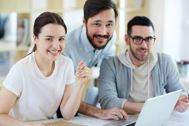 Группа успешных бизнесменов, работающих с ноутбуками в современном офисе, весело улыбающихся и смотрящих в камеру
 - Фото, изображение
