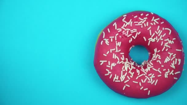 Delicious sweet donut rotating on a plate. Top view. Bright and colorful sprinkled donut close-up macro shot spinning on a blue background. - Footage, Video