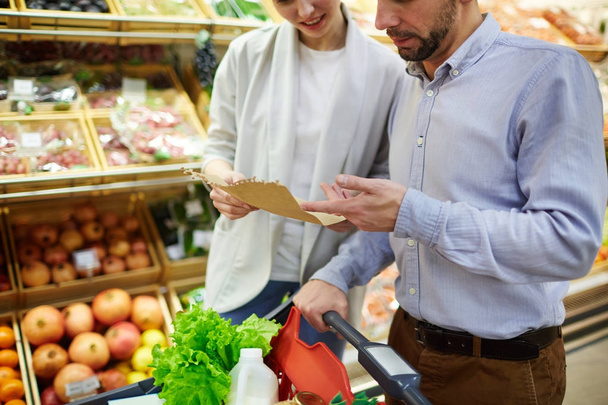 Young husband and wife discussing shopping list in supermarket - Photo, Image