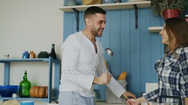 Happy young couple have fun dancing and singing in kitchen while listening to music in the morning at home - Materiał filmowy, wideo