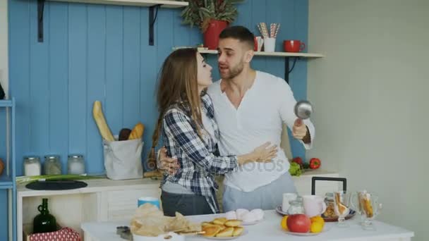 Joyful couple have fun dancing and singing in the kitchen at home in the morning - Felvétel, videó